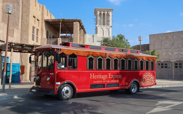 Red Heritage Express trolley in front of traditional Emirati architecture, Dubai.