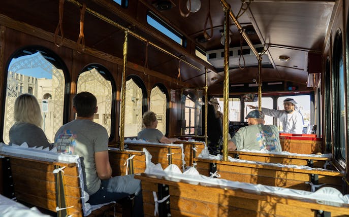 Tourists on a traditional Emirati trolley with a guide explaining local landmarks.