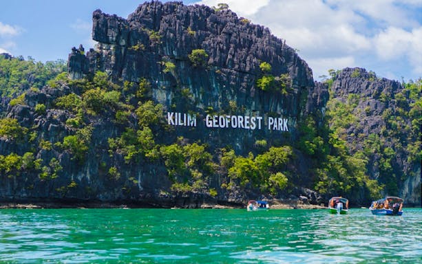 Langkawi Kilim Geoforest Park cliffs with boats on turquoise water.