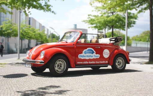 Red VW Beetle for 4-hour Berlin tour parked on cobblestone street.