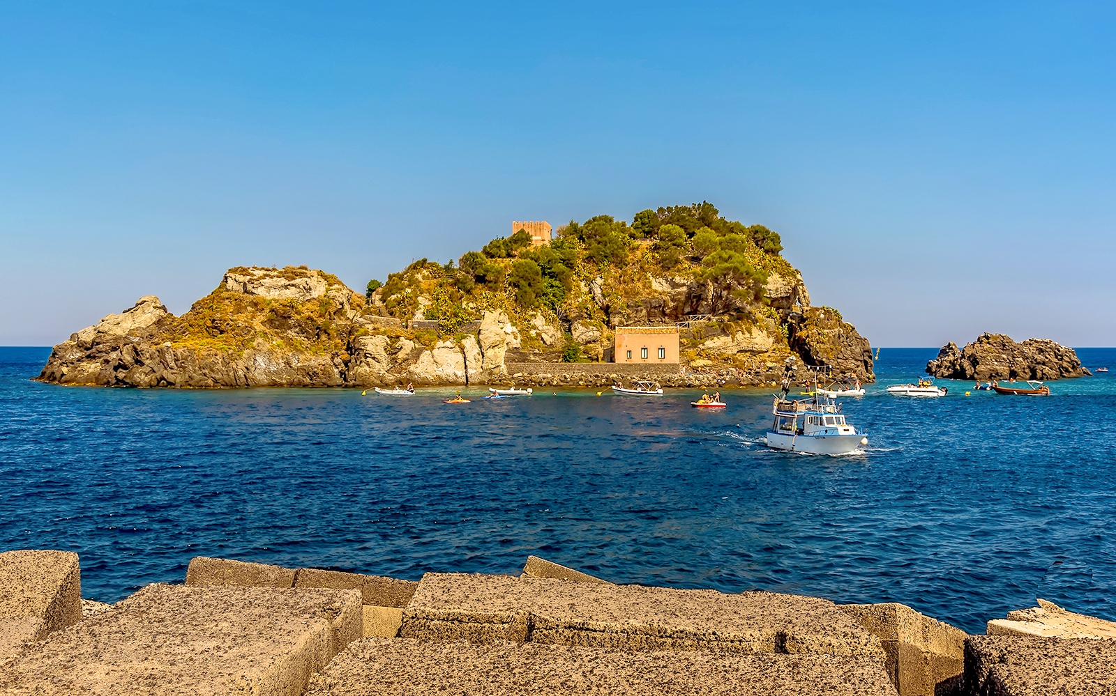 Snorkeling boats near Isole Ciclopi, Catania, with rocky island and clear blue sea.