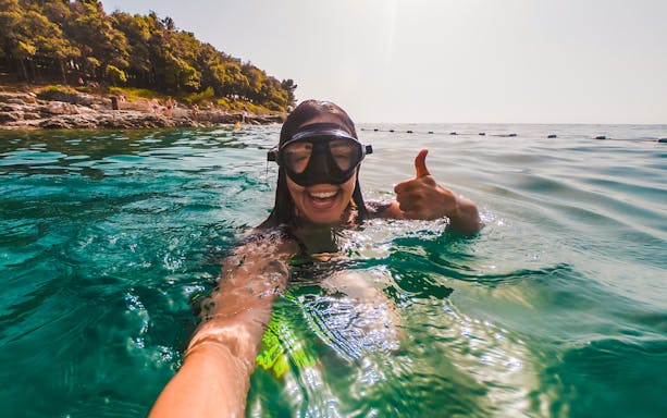Snorkeler giving thumbs up in clear waters near Isole Ciclopi, Catania.
