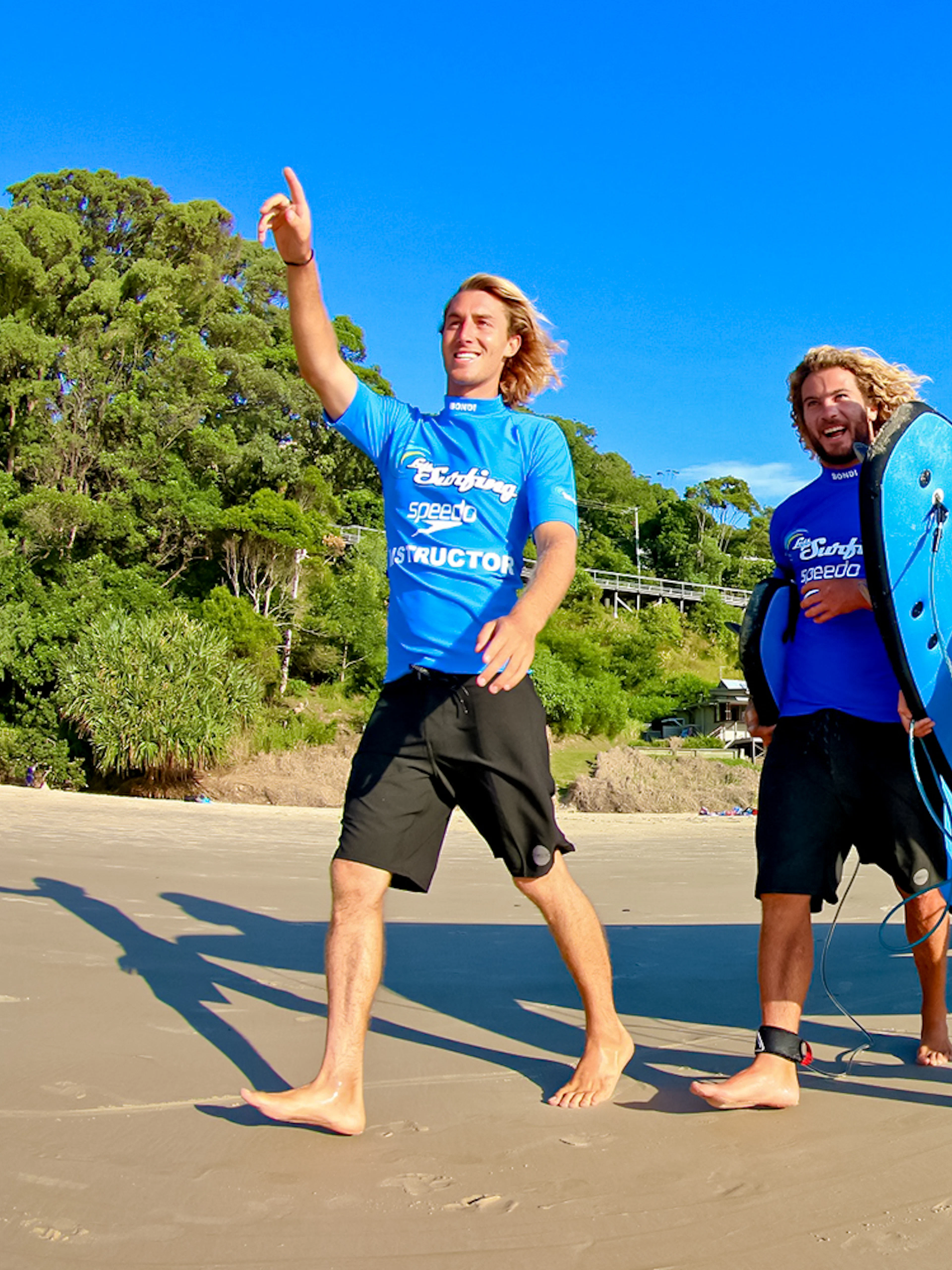 Surfers with boards walking on Byron Bay beach during a surf lesson.