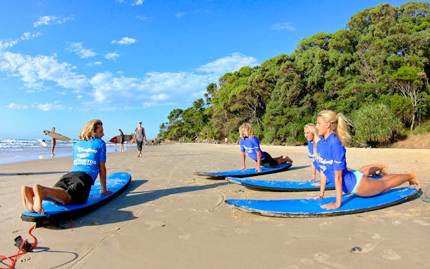 Surf instructor leading a lesson on Byron Bay beach with students on surfboards.