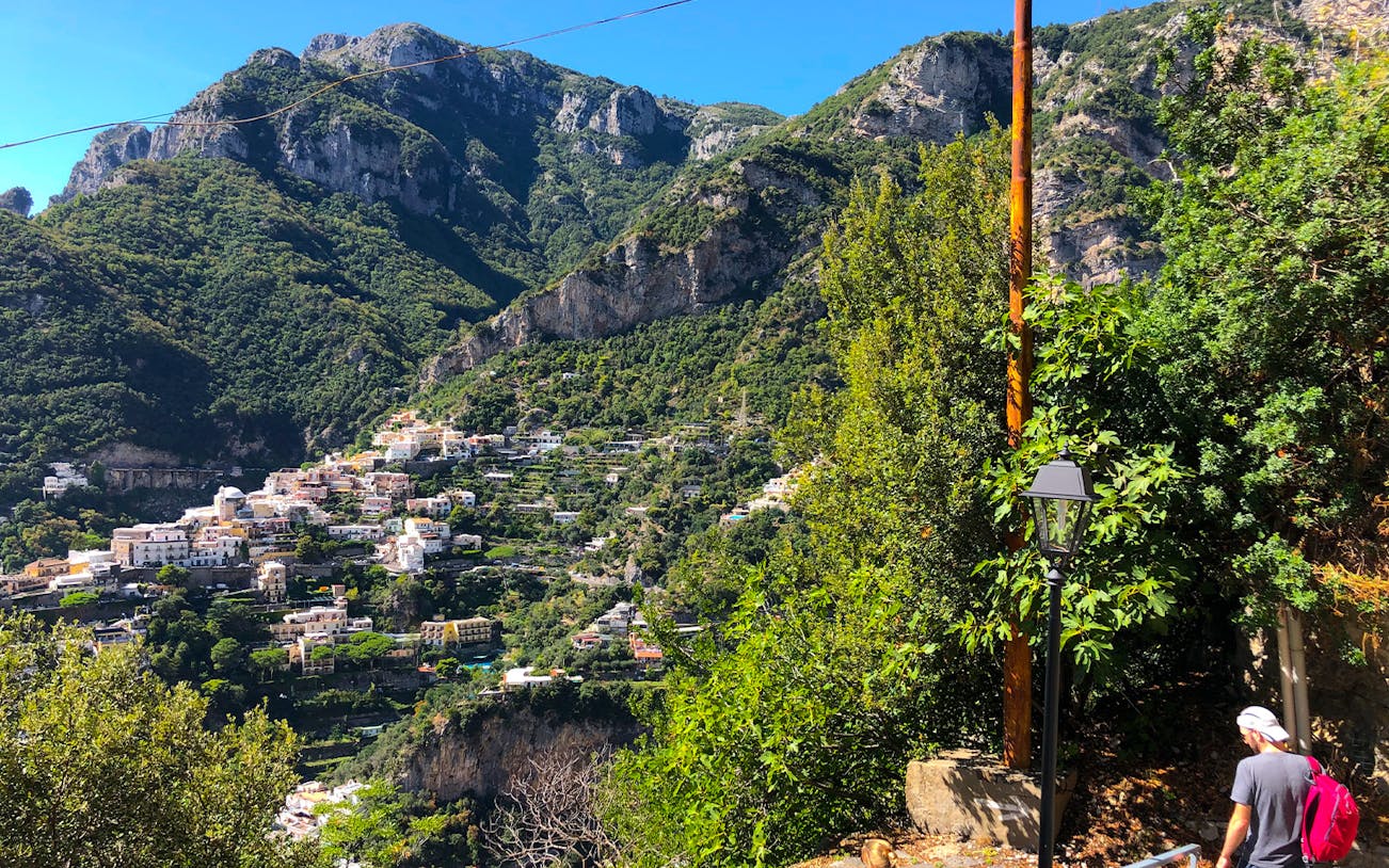 Hiker on Path of the Gods trail with view of Amalfi Coast village, Italy.