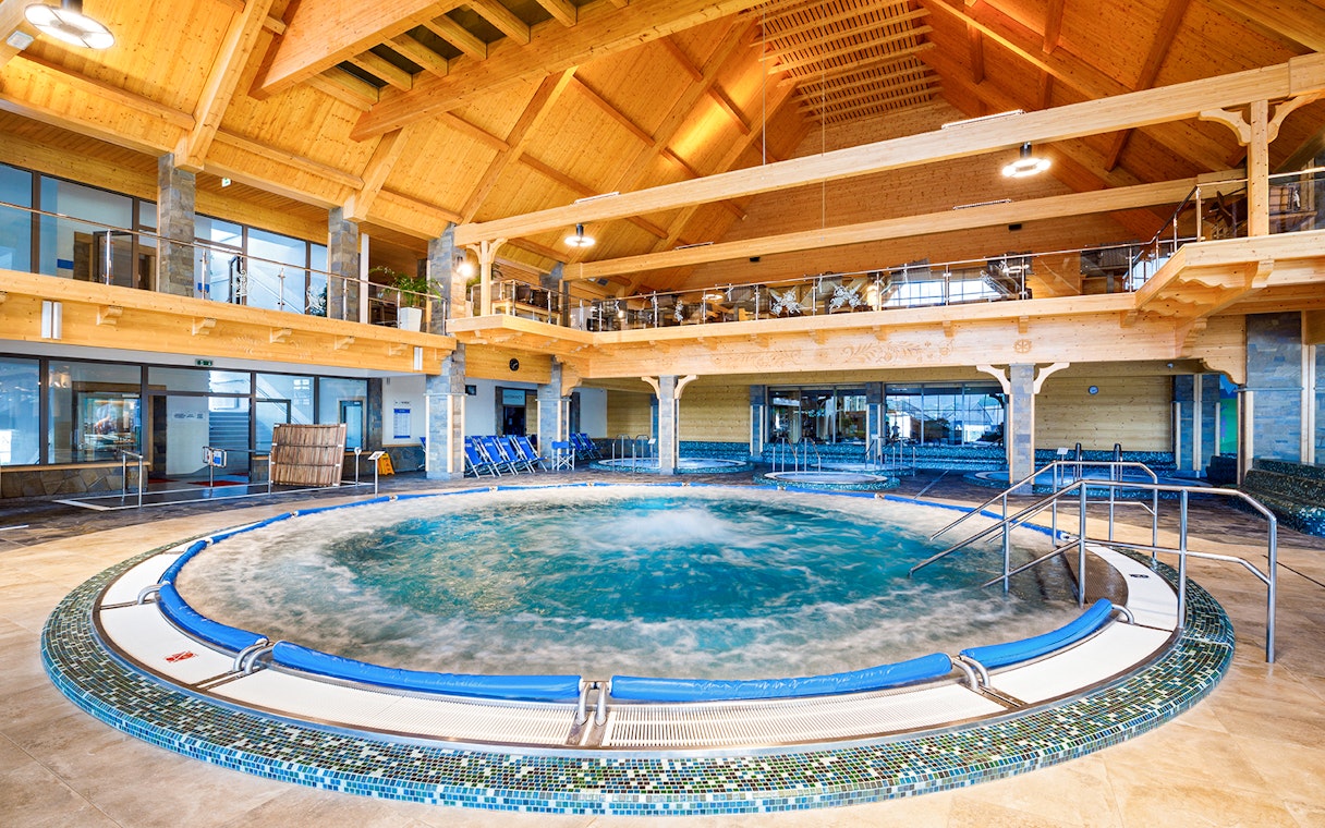 Indoor pool at Chocholow Thermal Baths with wooden ceiling and seating area.