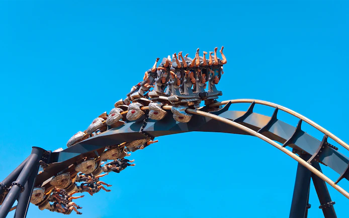 Roller coaster at Mirabilandia with riders upside down against a clear blue sky.