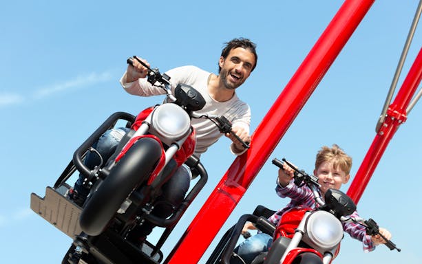 Father and son enjoying a motorcycle ride attraction at Mirabilandia, Italy.