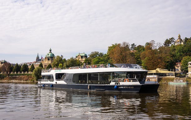 Electric boat on Prague river with historic buildings in the background.