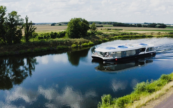 Electric boat cruising on a serene river in Prague, surrounded by lush greenery.