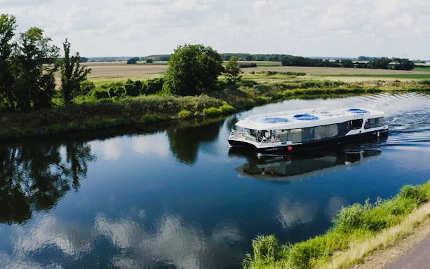 Electric boat cruising on a serene river in Prague, surrounded by lush greenery.