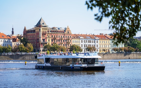 Electric boat cruising on the Vltava River in Prague with historic buildings in the background.