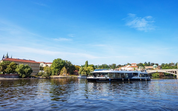 Prague river cruise boat on Vltava River with cityscape and bridge in background.