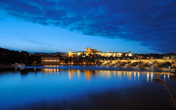 Prague Castle and Charles Bridge illuminated at night, view from river cruise.