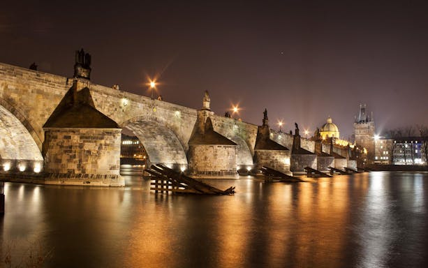 Charles Bridge illuminated at night over the Vltava River in Prague.