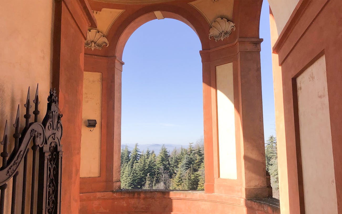 Arched portico view of trees and hills in Bologna during e-bike tour.