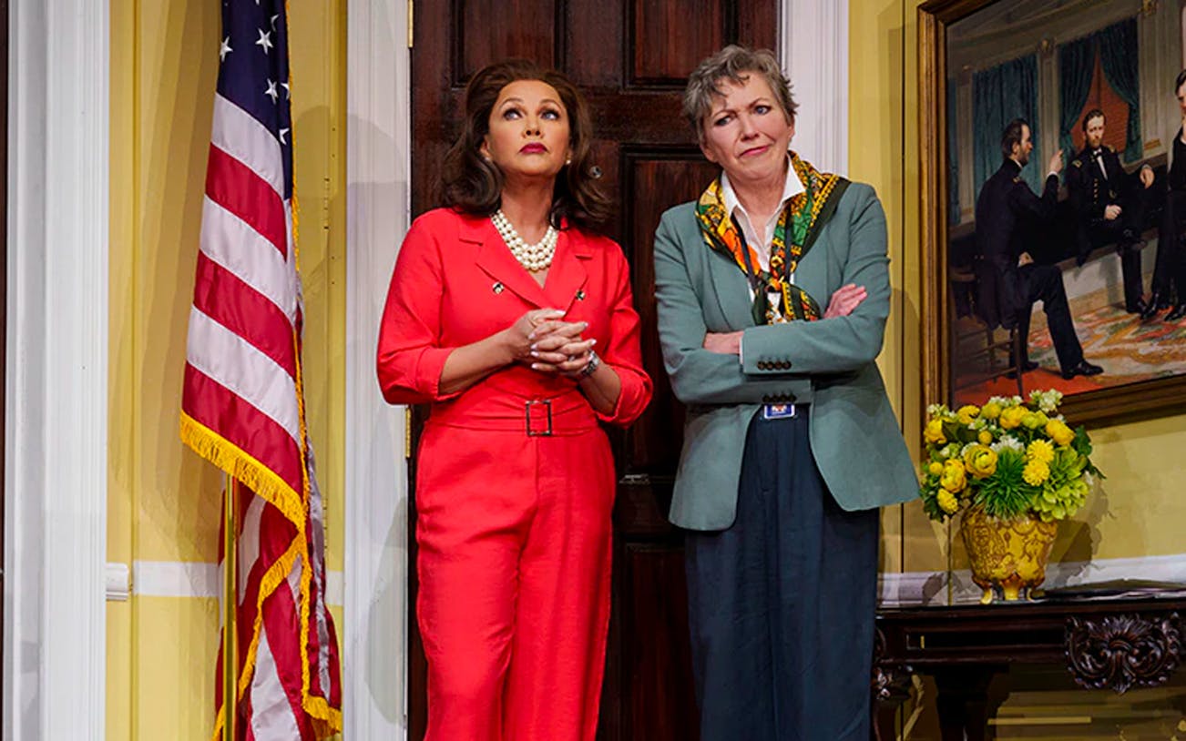 Two women standing in front of a door with an American flag and a historical painting.