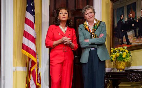 Two women standing in front of a door with an American flag and a historical painting.