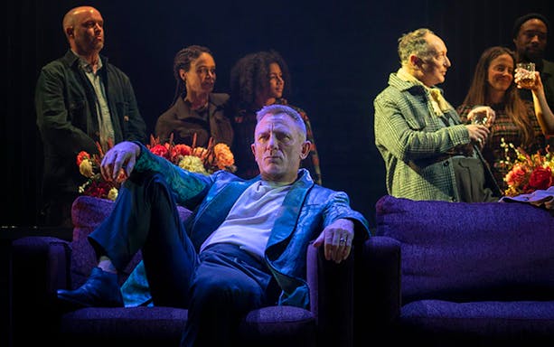 Actor seated on stage during a Macbeth performance, surrounded by cast members.