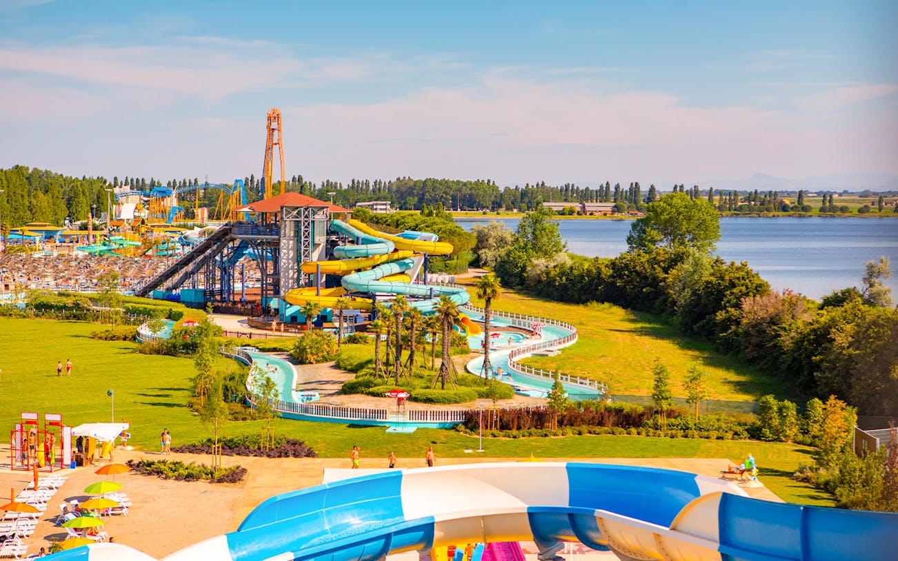 Water park with colorful slides and lazy river at Mirabeach, surrounded by greenery and a lake.