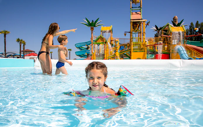 Children playing in a pool at Mirabeach water park with colorful slides in the background.