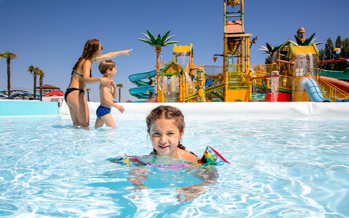 Children playing in a pool at Mirabeach water park with colorful slides in the background.