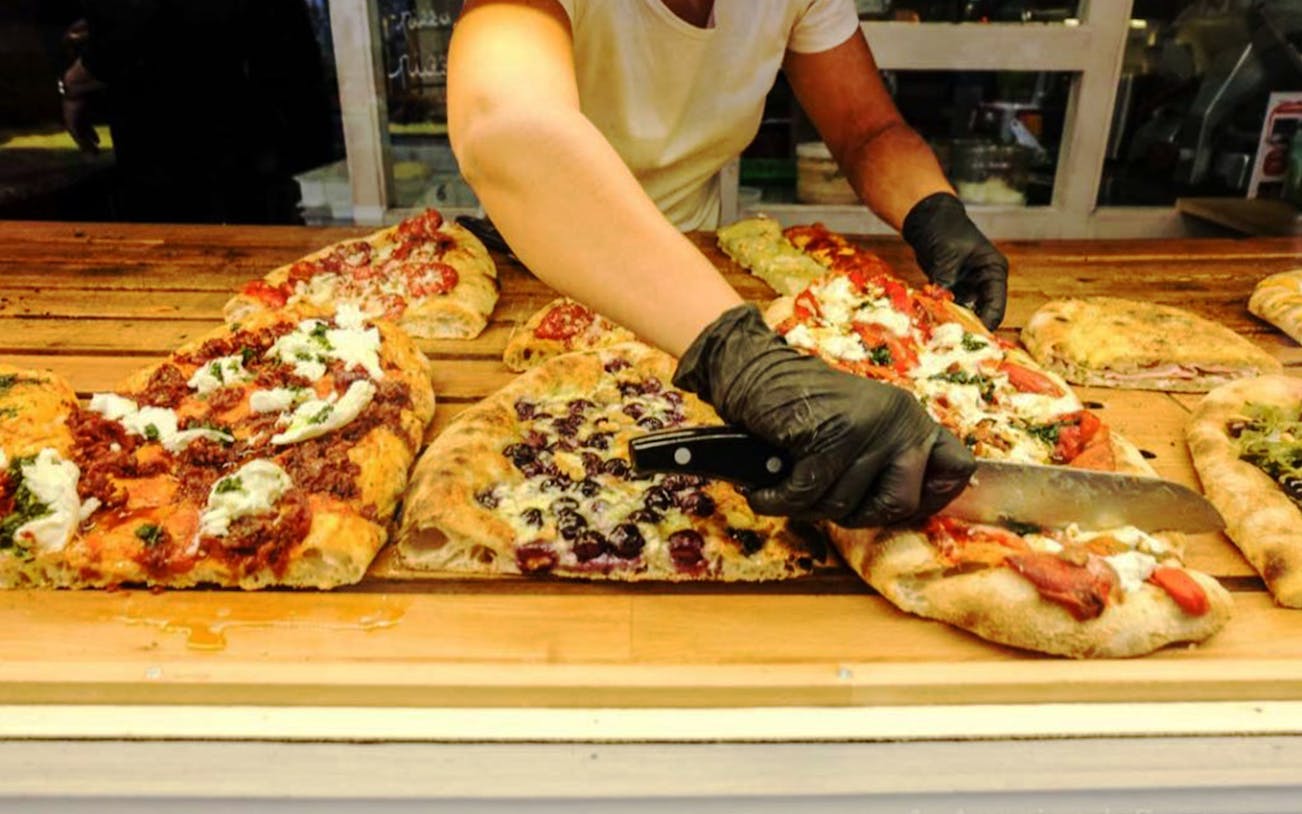 Pizza slices being cut at a food stall in Testaccio, Rome during an audio walking tour.