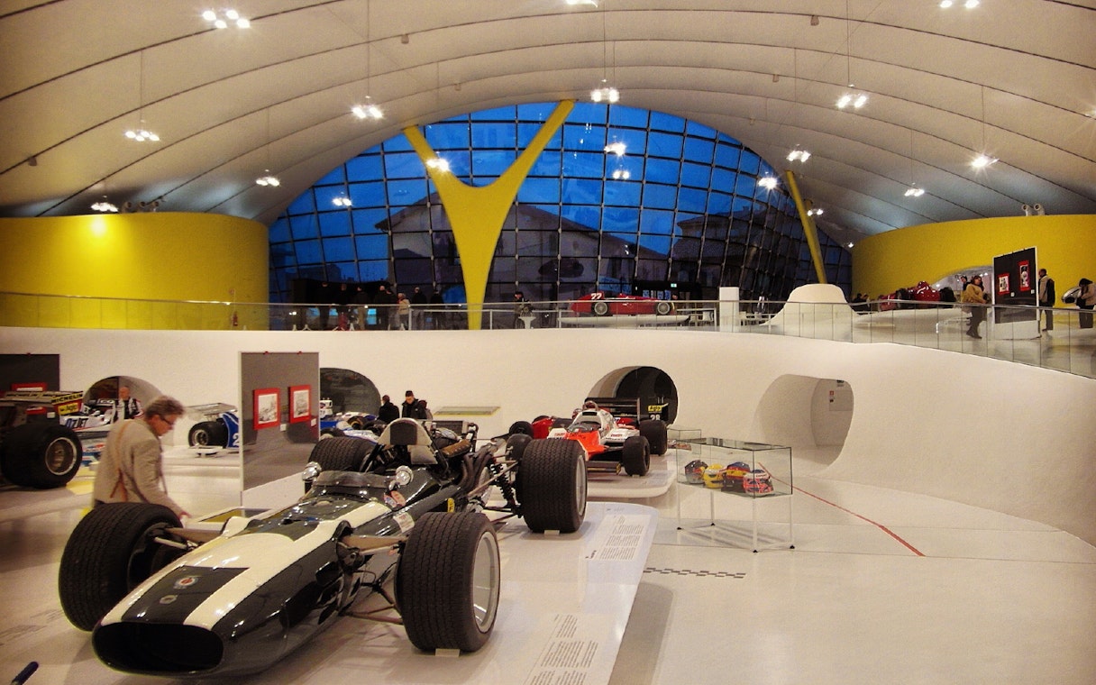Race cars displayed inside Museo Enzo Ferrari Modena with modern architecture.