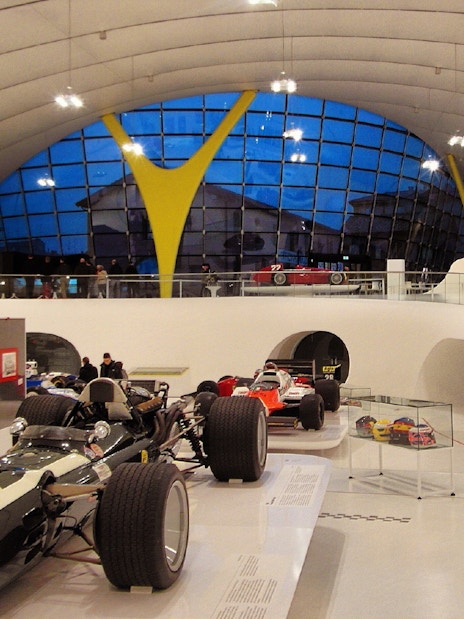 Race cars displayed inside Museo Enzo Ferrari Modena with modern architecture.
