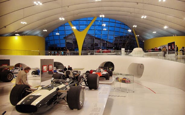 Race cars displayed inside Museo Enzo Ferrari Modena with modern architecture.