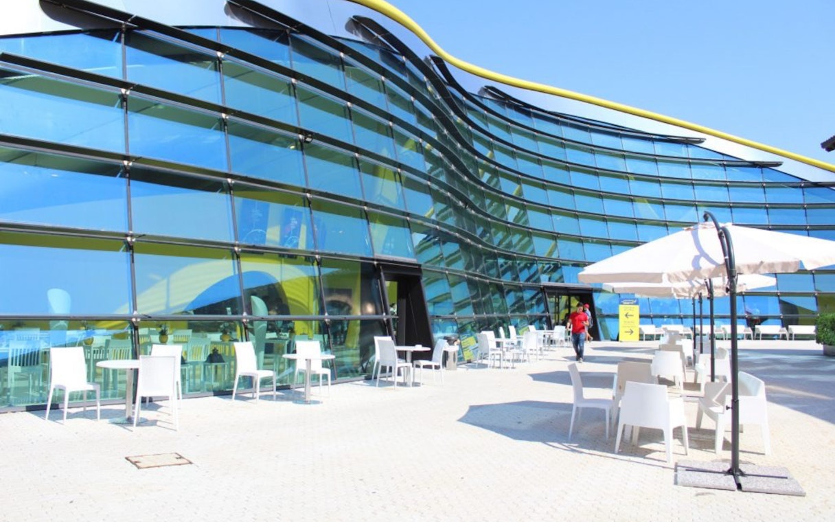 Exterior view of Museo Enzo Ferrari Modena with modern glass facade and outdoor seating.