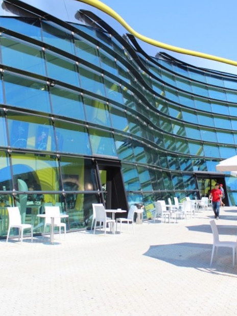 Exterior view of Museo Enzo Ferrari Modena with modern glass facade and outdoor seating.