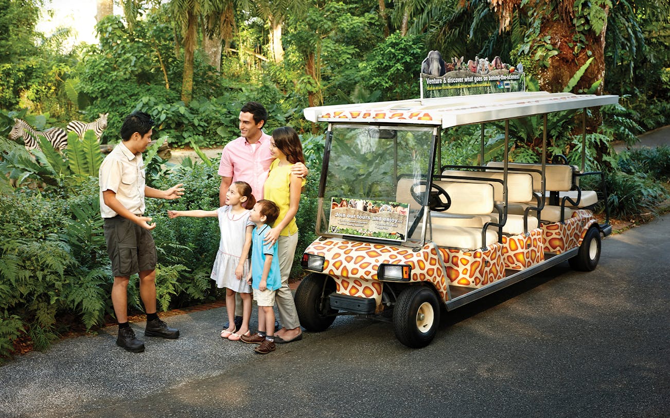 Family with guide near safari tram at Singapore Zoo.