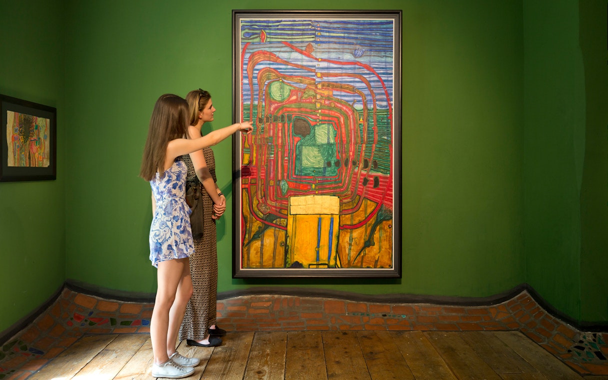 Visitors observing a colorful painting at KUNST HAUS WIEN, Hundertwasser Museum exhibit.