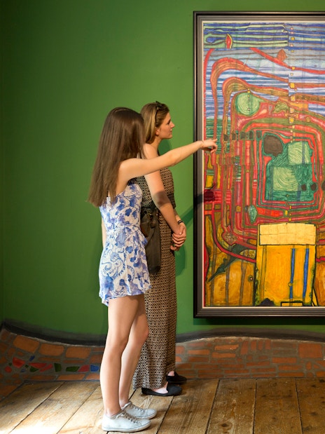 Visitors observing a colorful painting at KUNST HAUS WIEN, Hundertwasser Museum exhibit.