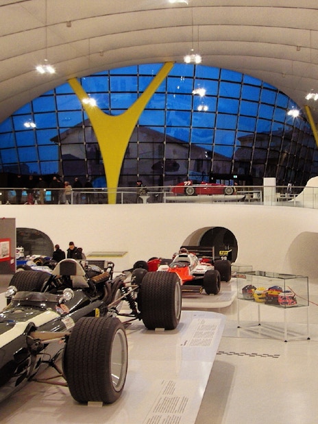 Ferrari race cars displayed at Modena Enzo Ferrari Museum with visitors exploring exhibits.