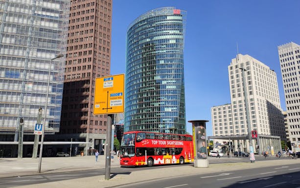 Red sightseeing bus at Potsdamer Platz, Berlin, with modern buildings in the background.