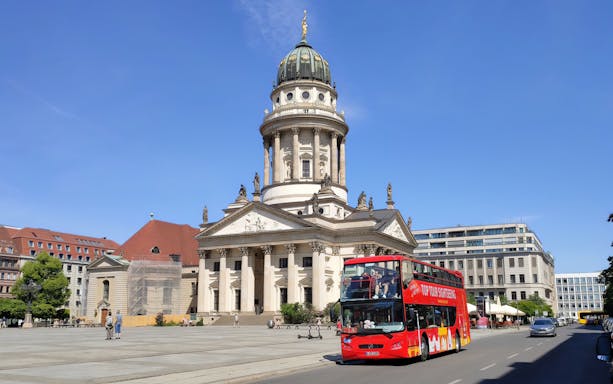 Red sightseeing bus in front of the French Cathedral, Berlin, on a sunny day.