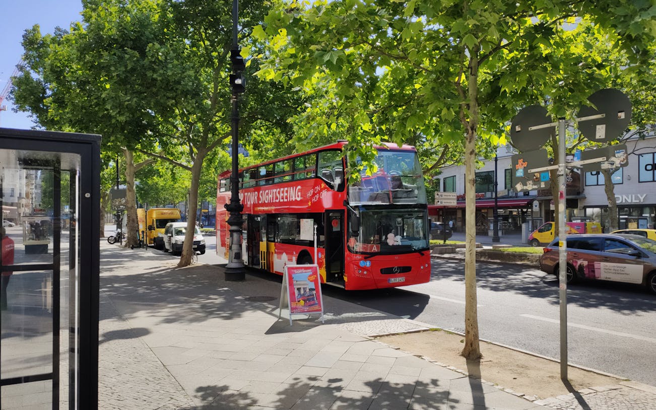 Red double-decker bus for Berlin hop-on hop-off tour parked on a tree-lined street.