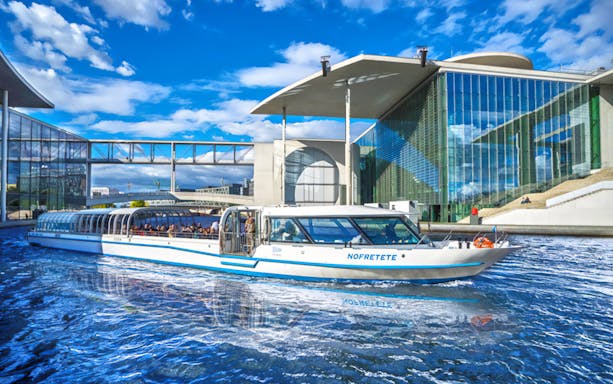 Berlin sightseeing boat near modern glass building on Spree River.