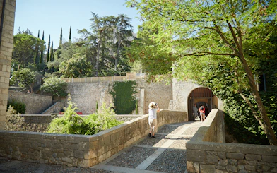 Stone bridge leading to historic entrance in Girona, surrounded by lush greenery.