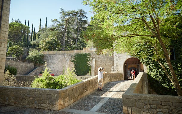 Stone bridge leading to historic entrance in Girona, surrounded by lush greenery.