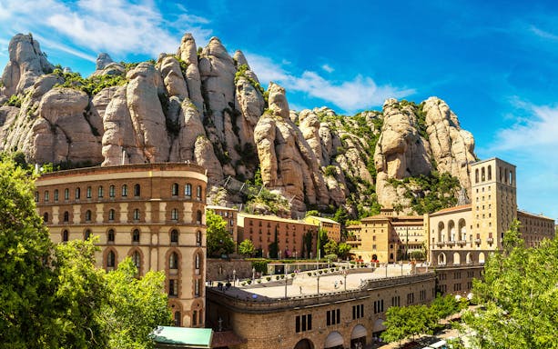 Montserrat Monastery with rocky mountain backdrop under blue sky.