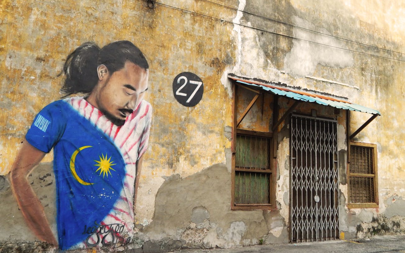 Street art mural in Georgetown, Penang, featuring a man in a Malaysian flag shirt on a weathered wall.