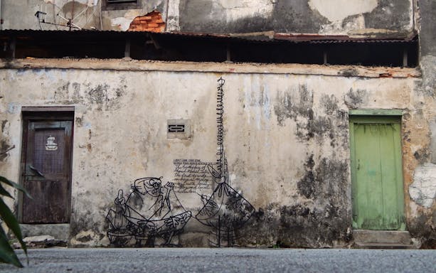 Street art on a weathered wall in Georgetown, Penang, depicting local culture.