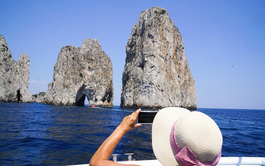 Person photographing Faraglioni rock formations from a boat on Capri Island tour.
