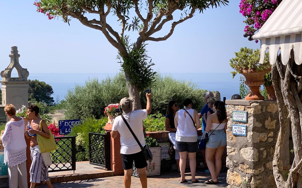 Tourists exploring Capri Island with a view of the sea and lush greenery.