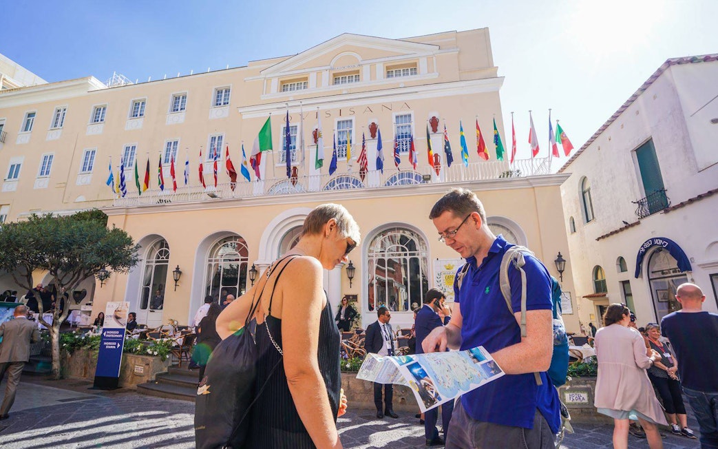 Tourists with a map in front of a building with flags on Capri Island.