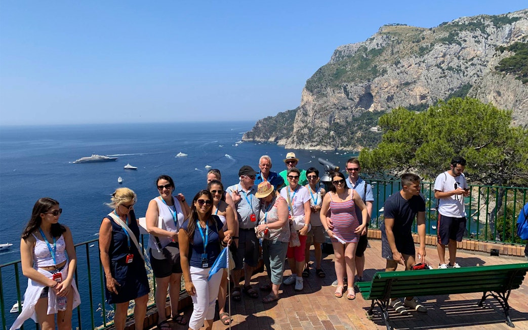 Tour group enjoying a scenic view of Capri Island cliffs and sea during a guided tour with boat ride.