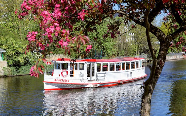 Tour boat on Alster River surrounded by blooming trees in Hamburg.